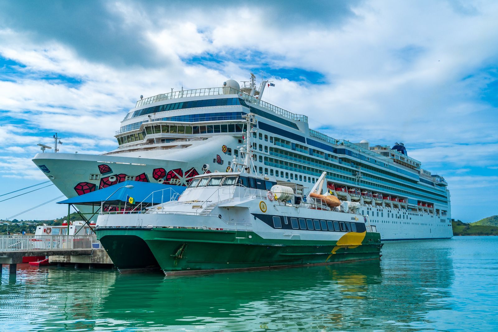 A cruise ship and a ferry moored side by side in turquoise water, a reminder of cheap cruise tips