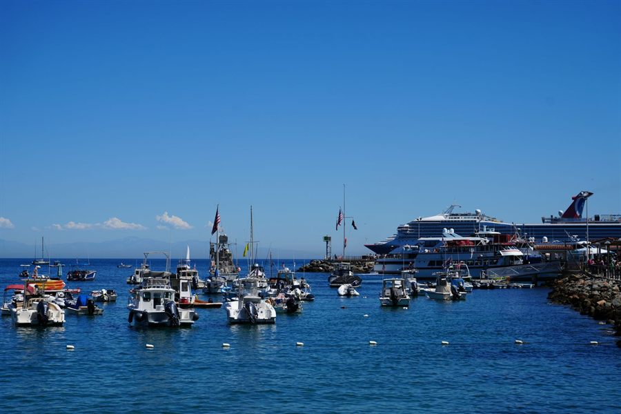 Small boats moored in a blue harbour with a cruise ship in the distance
